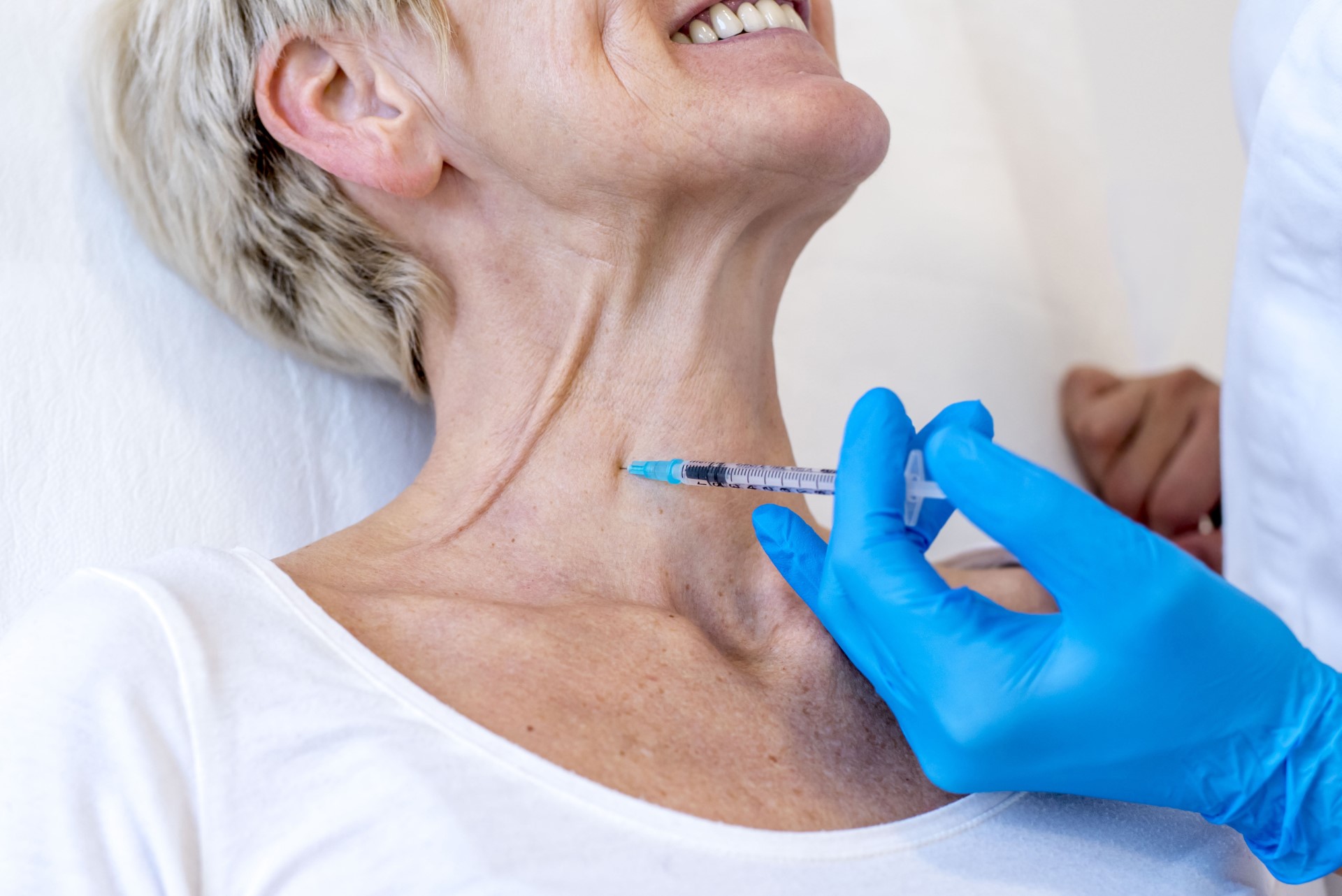 A closeup of a cheerful old female getting Botox in her neck.
